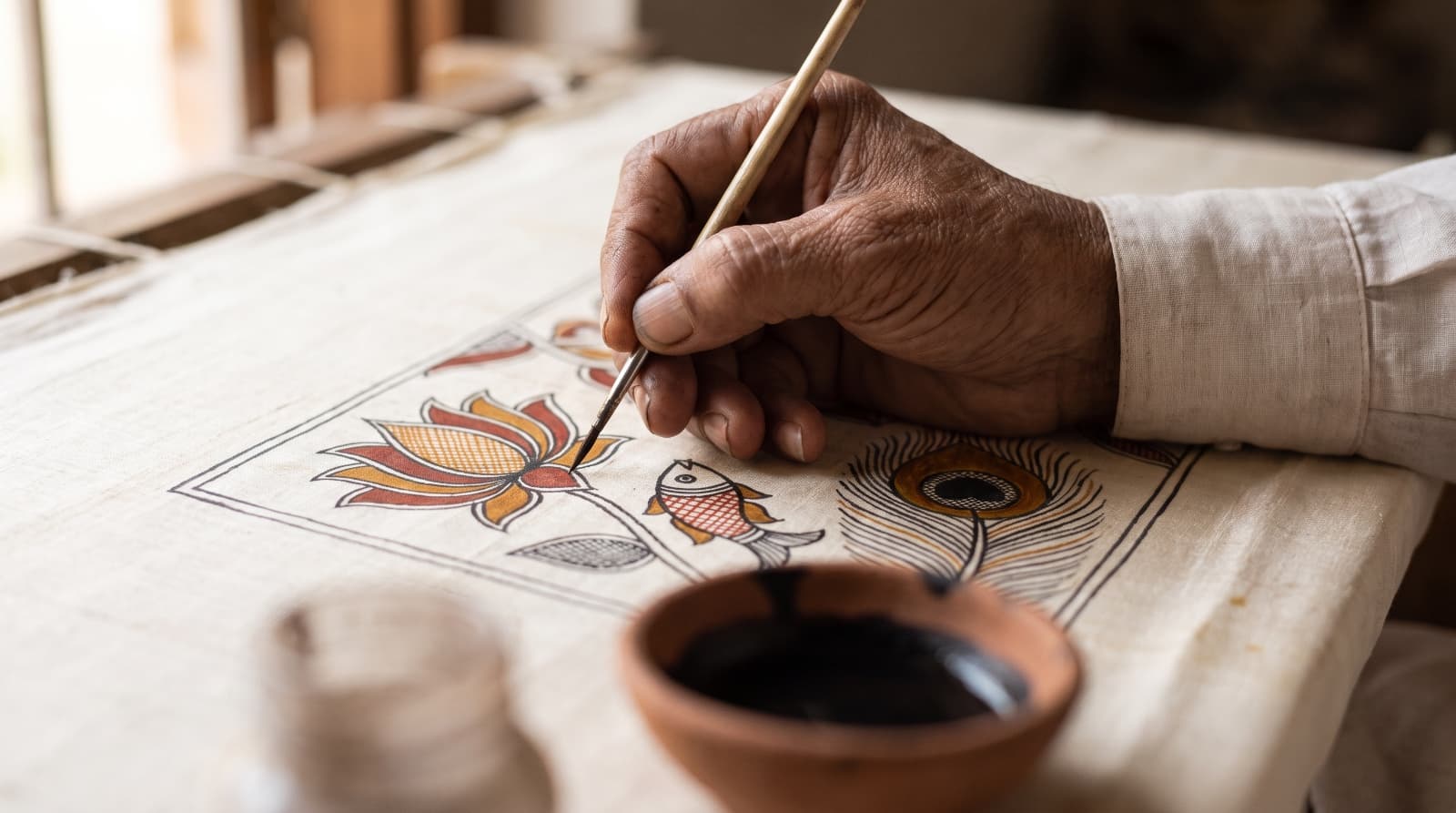An artisan's hand filling natural colour into a Madhubani motif on silk