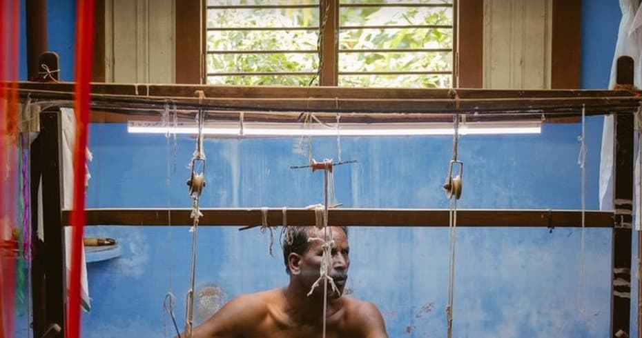 A weaver working a handloom, threads strung between wooden beams