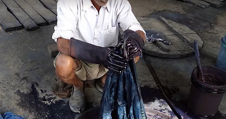 An artisan hand-dyeing cloth in indigo, lifting it from the dye bath
